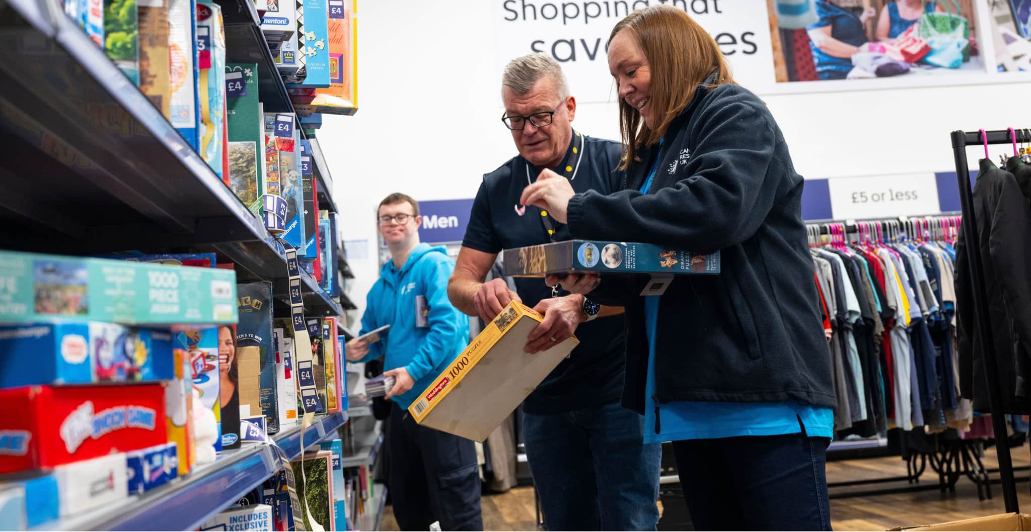 Three shop volunteers sorting jigsaws ready to put on the shelves within a Cancer Research UK shop.
