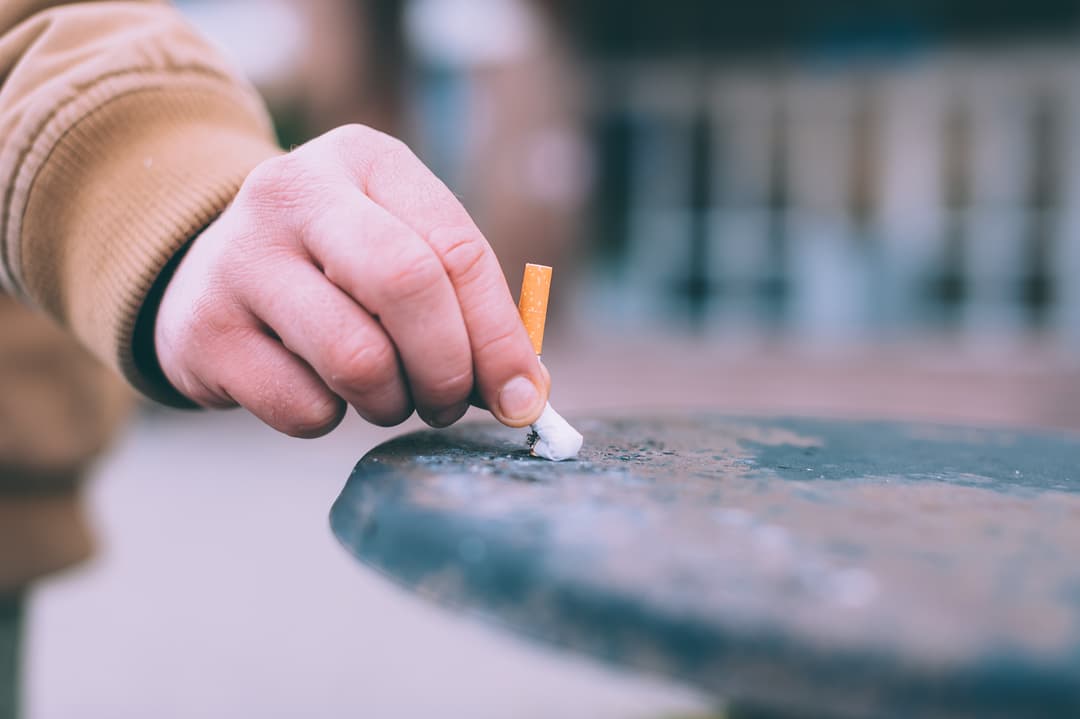A man puts out a cigarette in the trash.