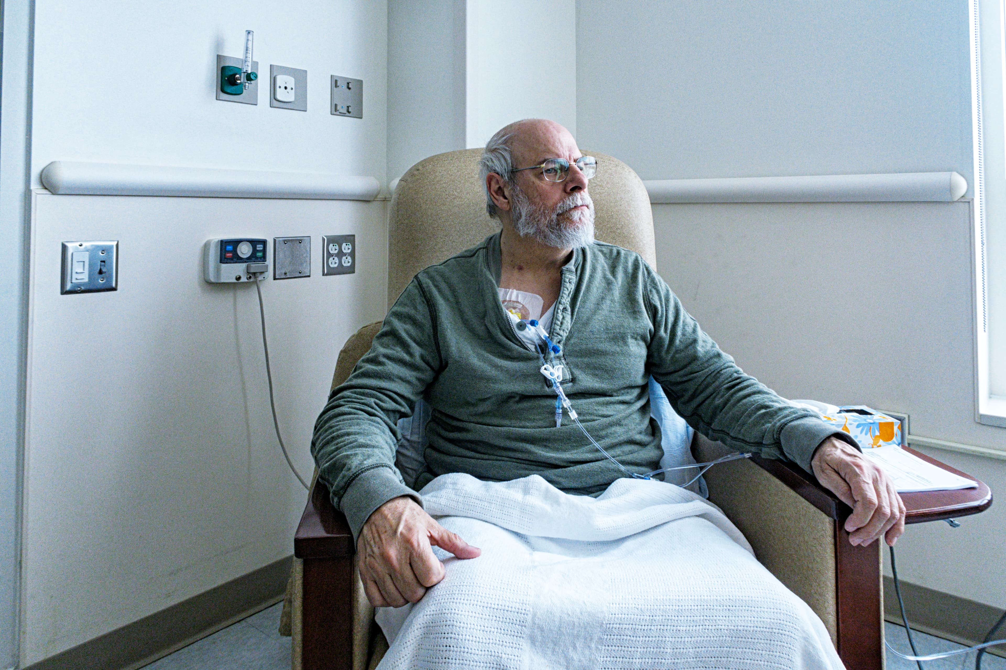 A patient having treatment, sitting on a chair with a white blanket.