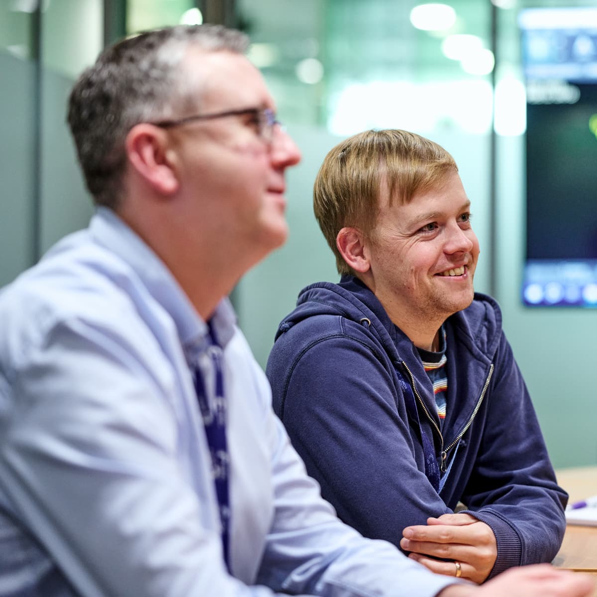 Two people sat at a table with a computer screen displaying a scientific image in the background.