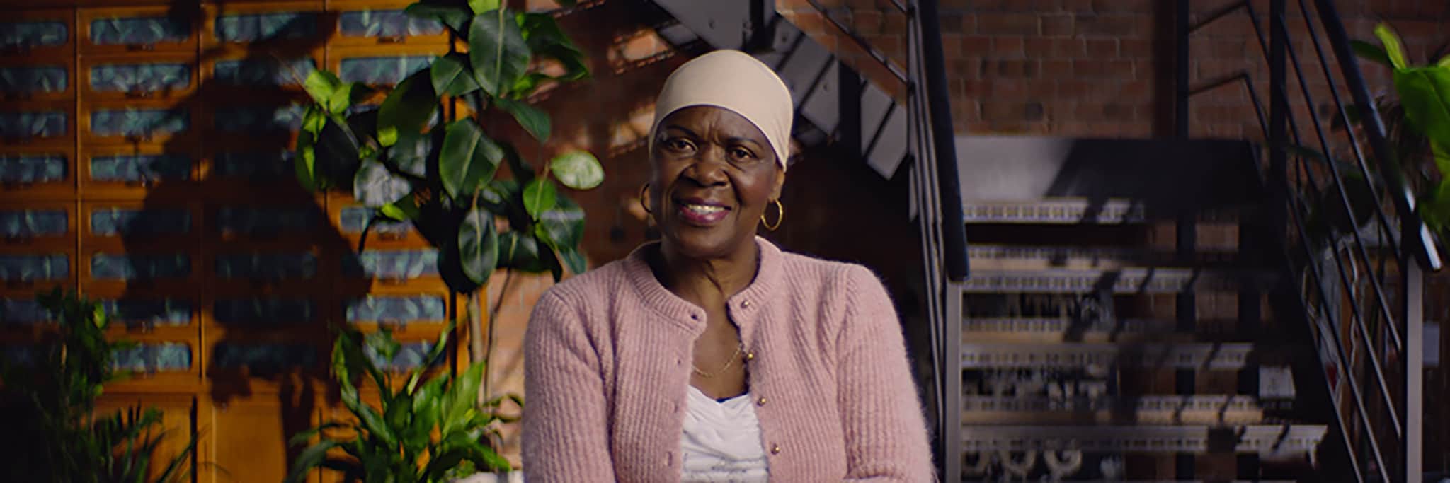 Photo of one of our media volunteers, Lauren Sky who is smiling and sitting in a sun-lit room with plants around her.