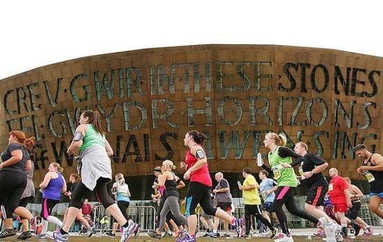 A large group of runners, running in front of the iconic Wales Millennium Centre in Cardiff Bay