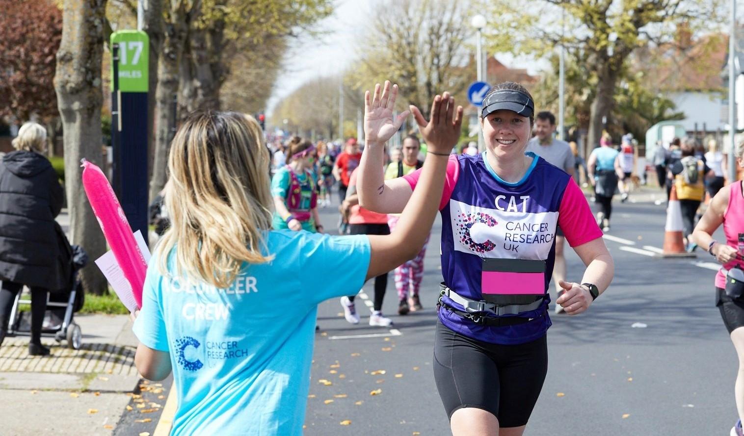 Woman running for CRUK high fiving a volunteer