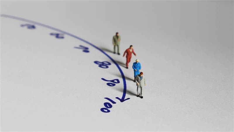 A stock image illustrating the ageing process with four people figurines alongside an arrow timeline up to 100 years old.